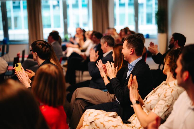 Publiek zit in rijen en applaudisseert tijdens een evenement