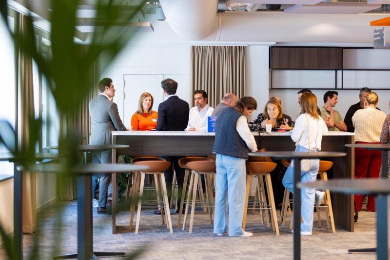 Mensen staan en praten informeel rond een hoge tafel tijdens een receptie